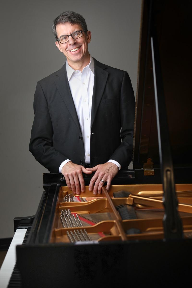 David DeMotta smiling, hands resting on the open lid of a grand piano