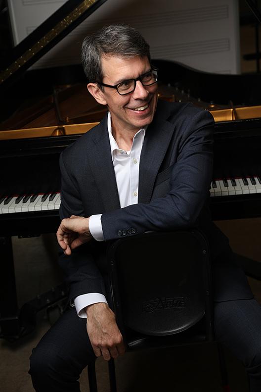 David DeMotta seated at a grand piano, laughing