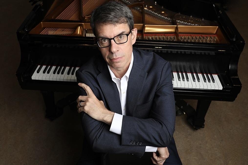 David DeMotta at a grand piano, arms crossed