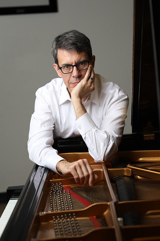 David DeMotta leaning on a grand piano, chin resting on his hand
