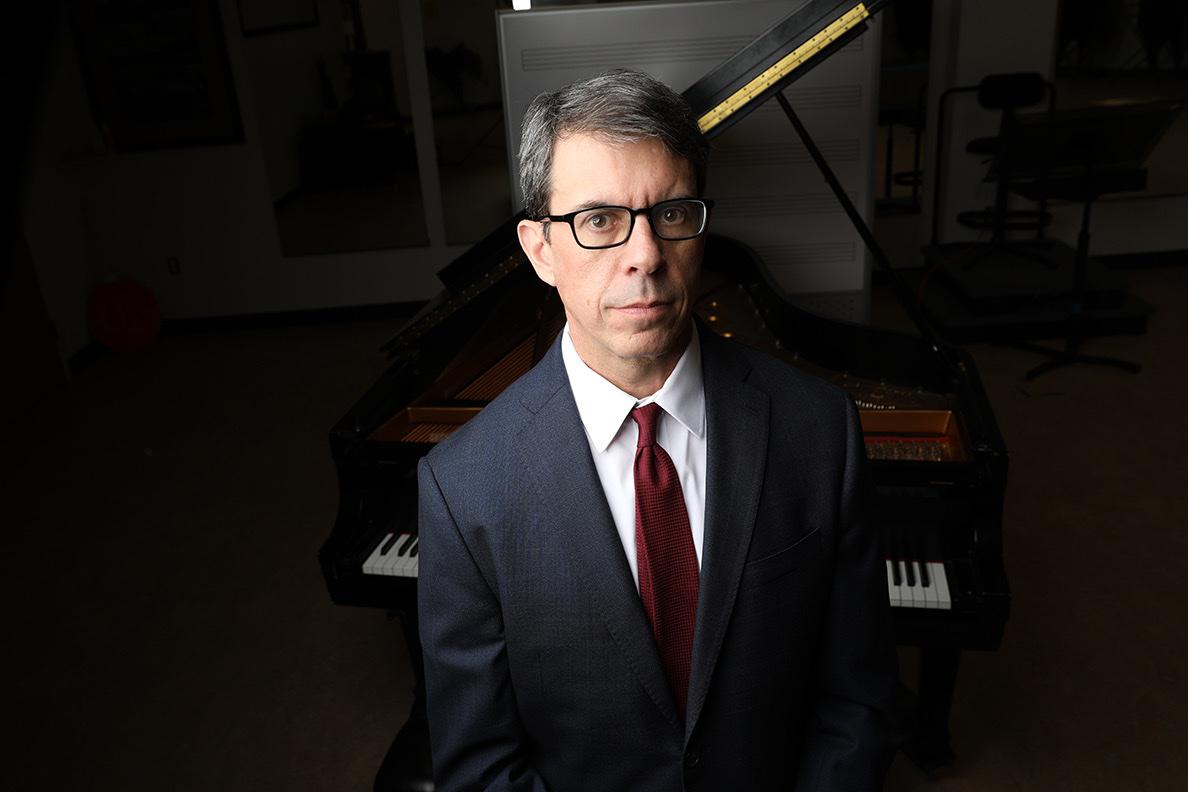 David DeMotta in a suit and red tie in front of a grand piano