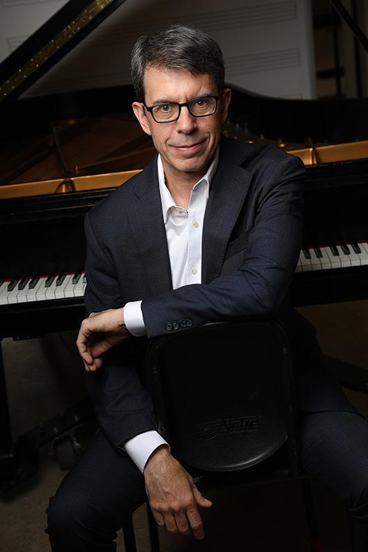 David DeMotta seated at a grand piano, arms resting on a chair back